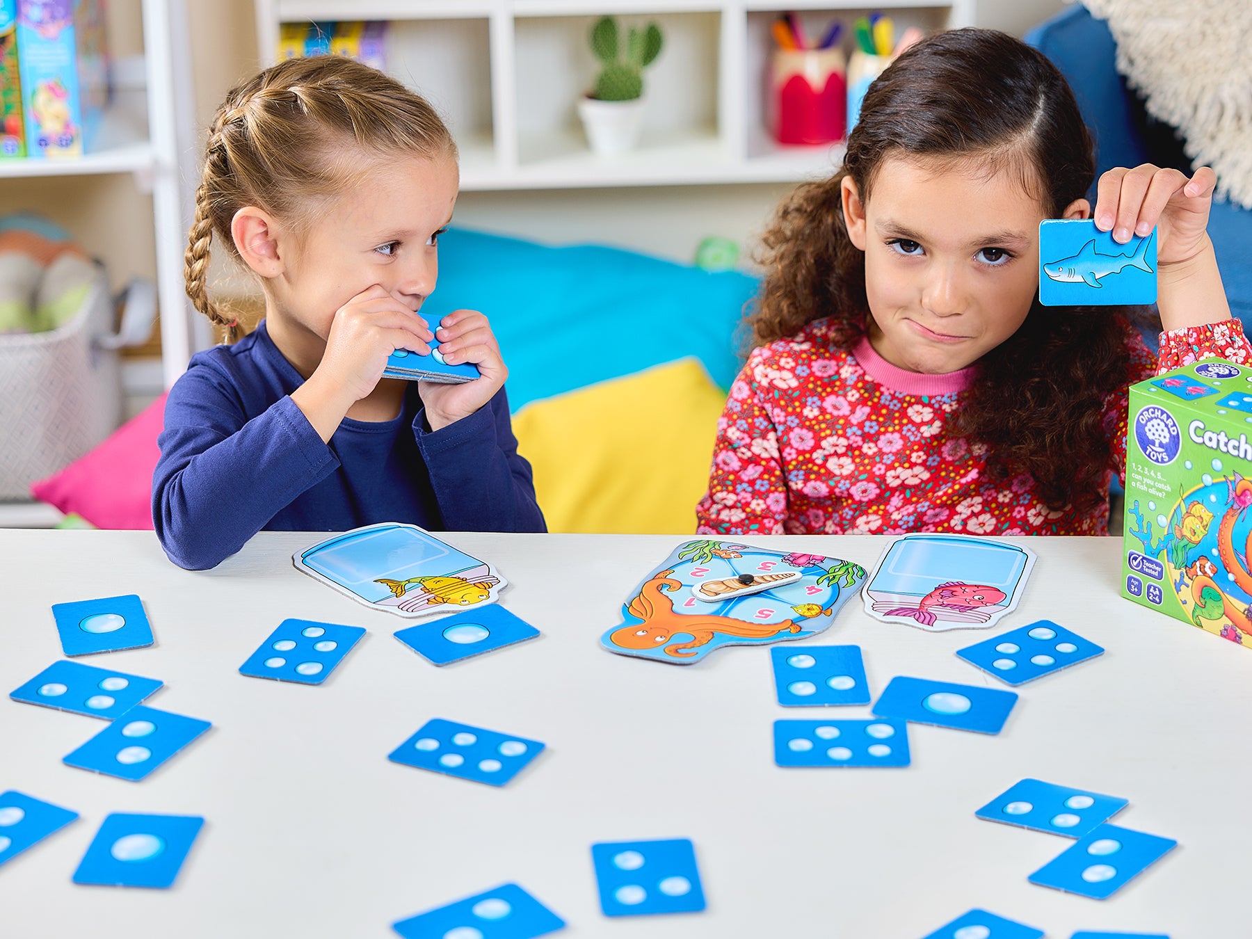 Two children playing with educational card games on a table in a colorful room.