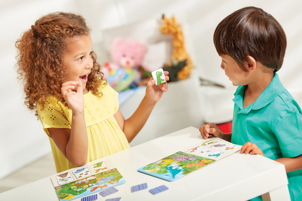 Two children playing with colorful cards at a table in a bright room.