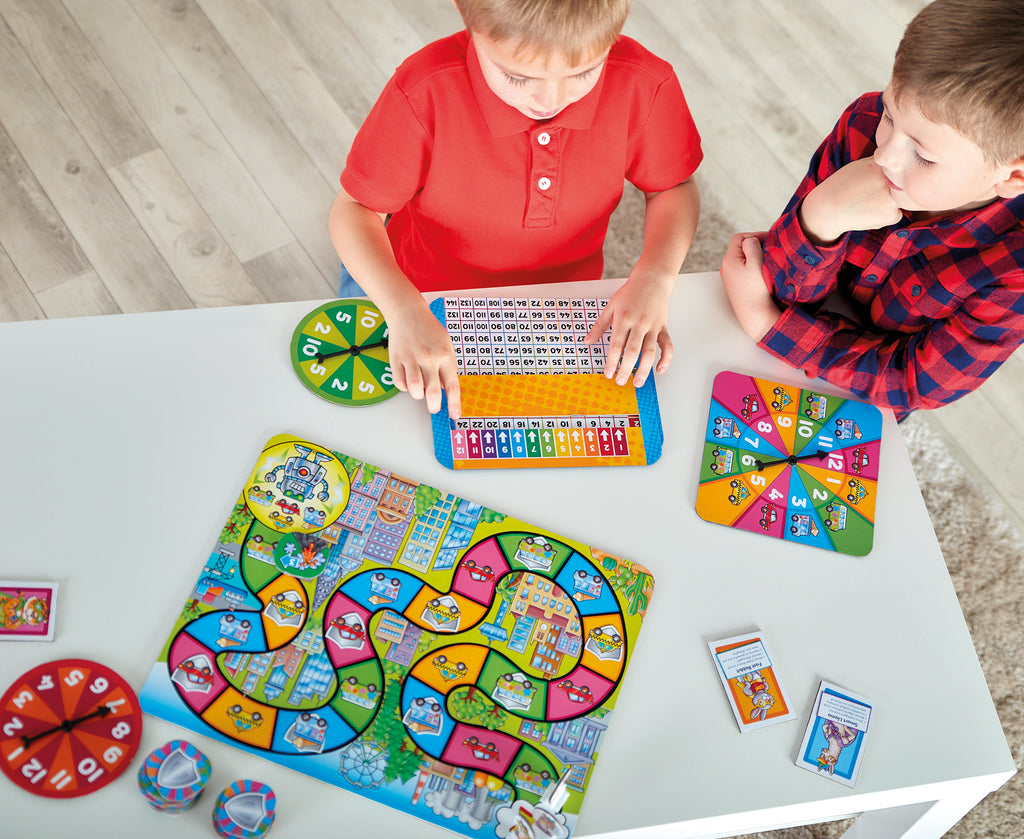 Two children playing with a colorful board game on a wooden floor.