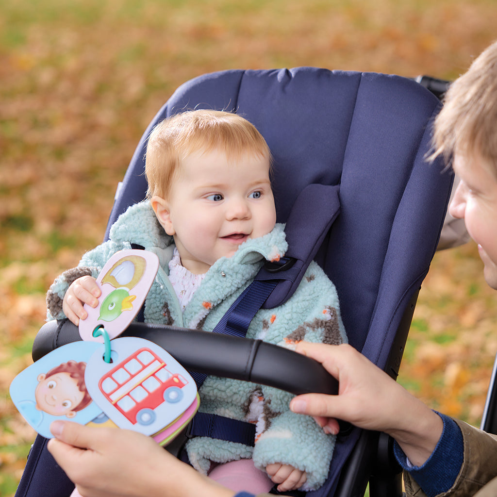 Child in a stroller with a baby, holding colorful cards outdoors.