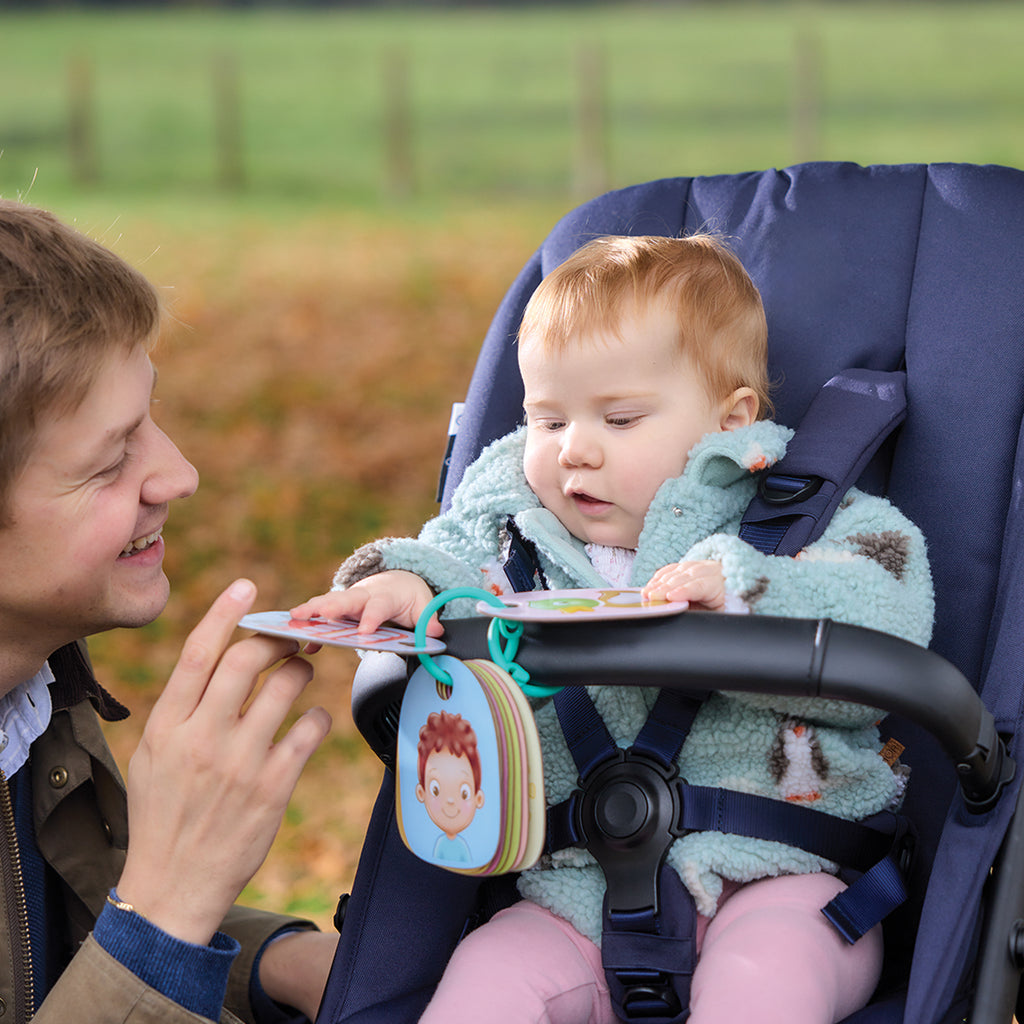 Man showing a book to a baby in a stroller outdoors