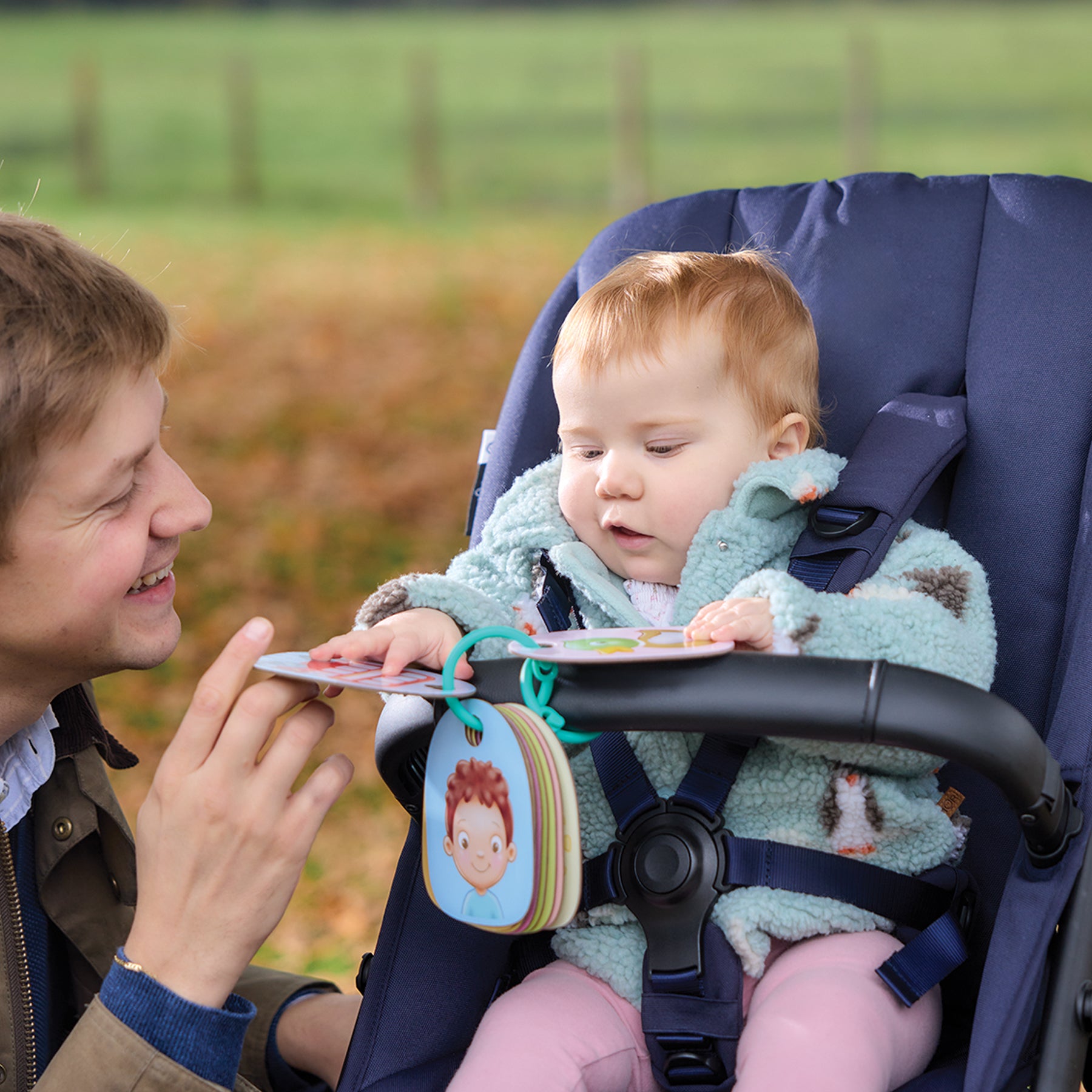 Man showing a book to a baby in a stroller outdoors