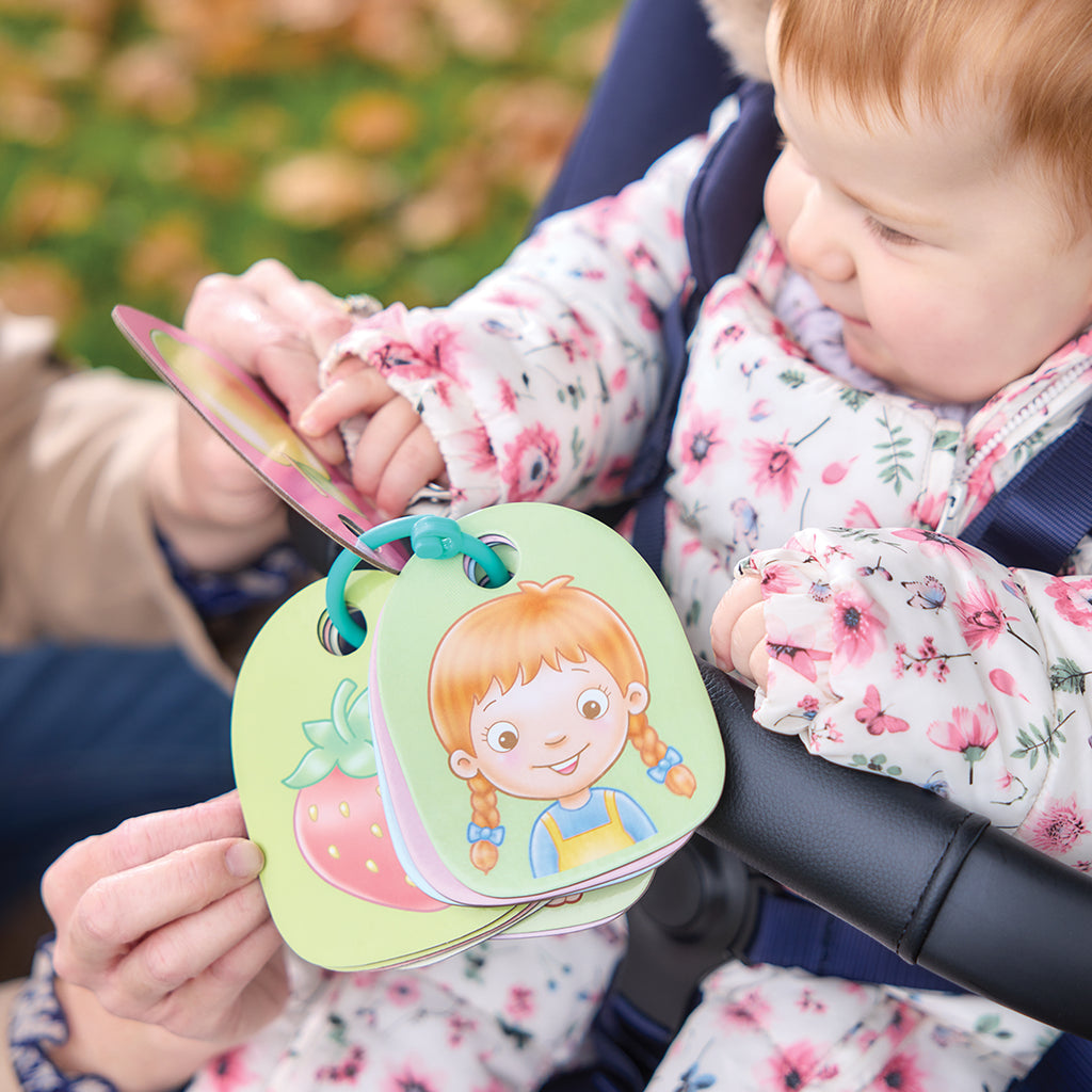 Child in a floral jacket holding a colorful book with a character on a green background.