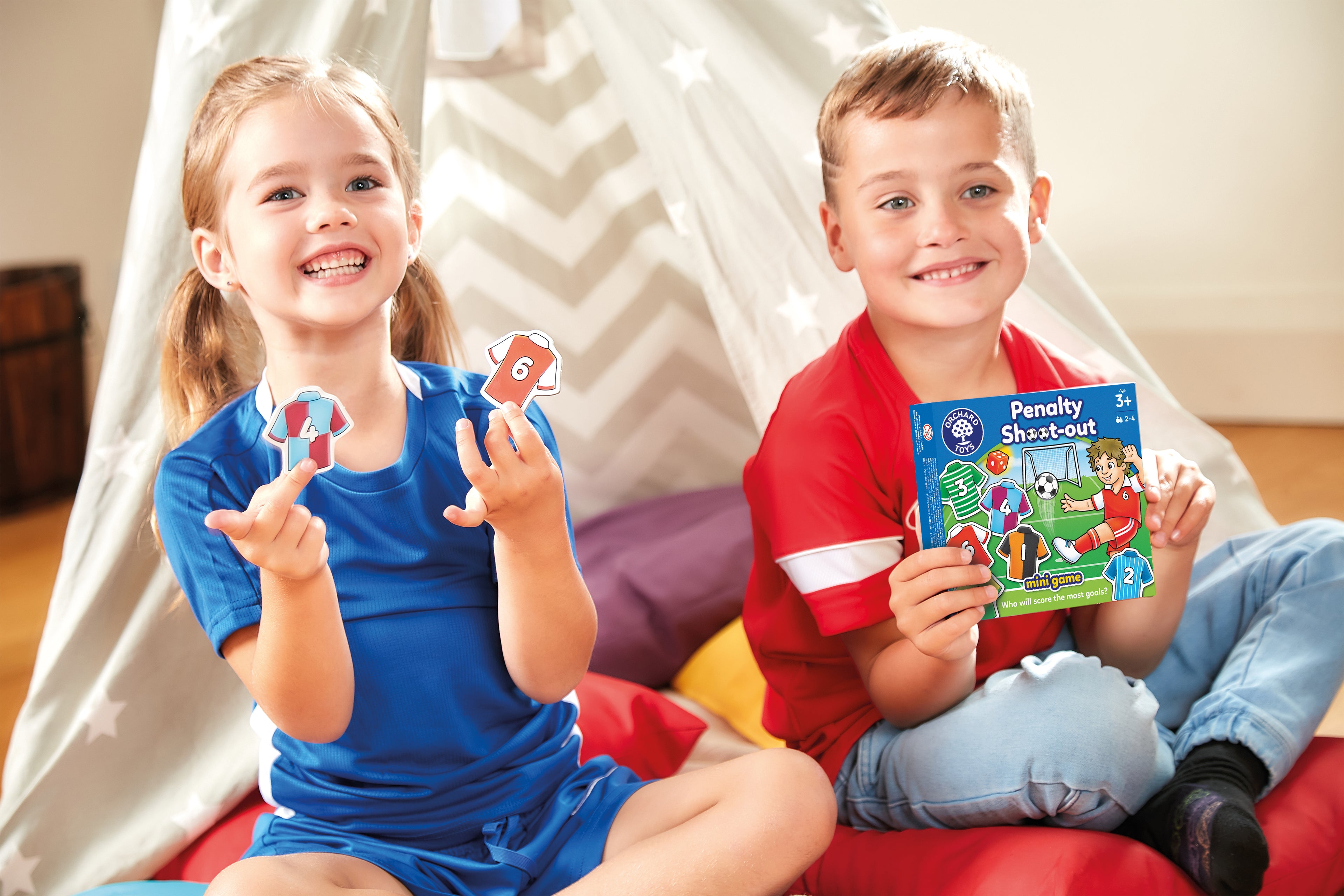Two children sitting on a red couch holding educational games and books.