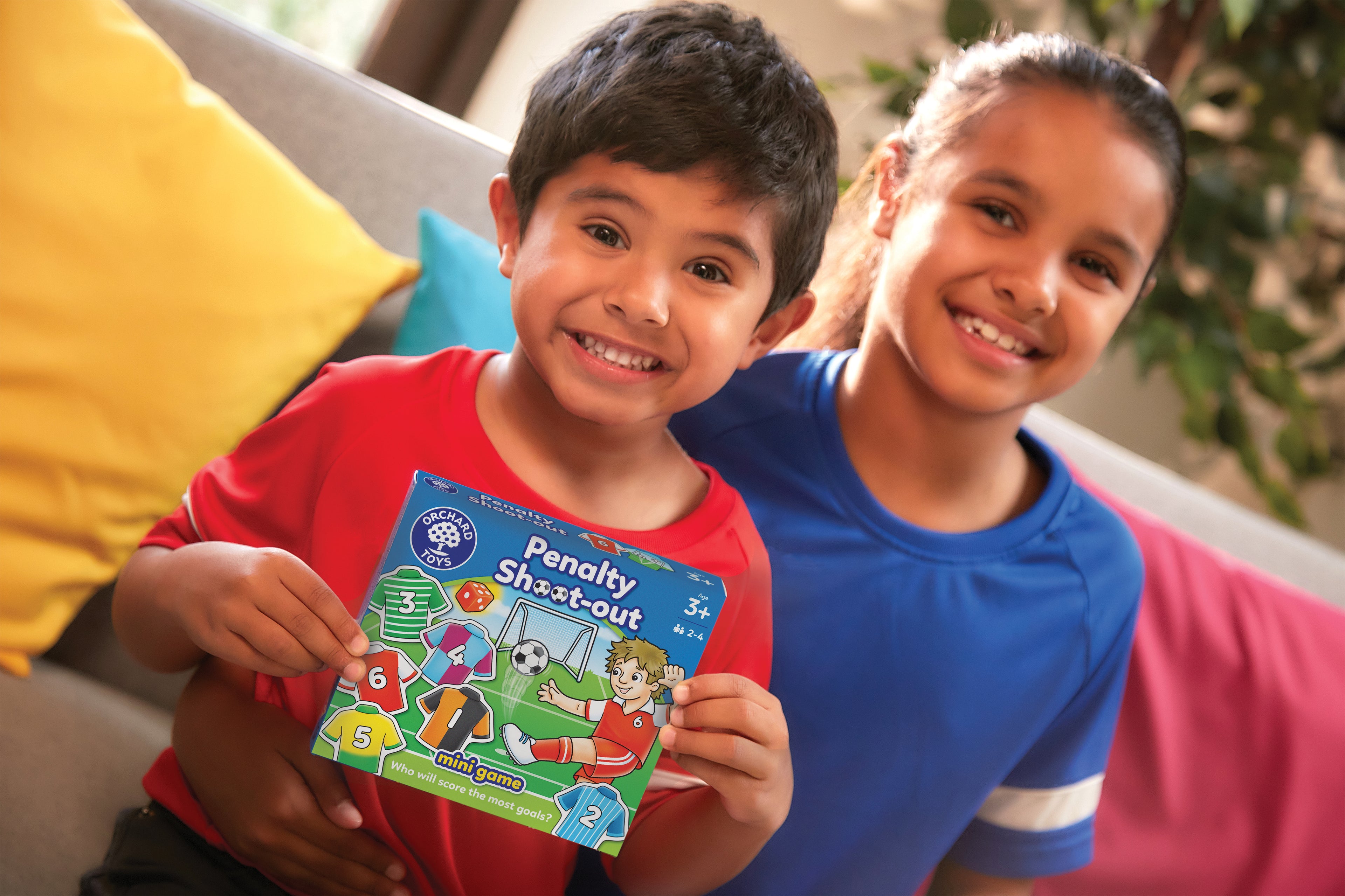 Two children holding a book titled 'Penalty Shootout' on a couch.