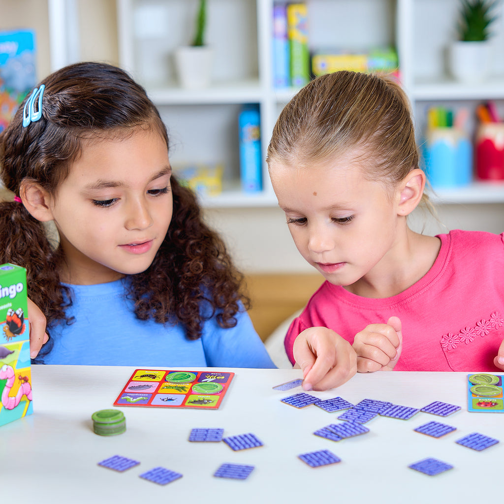 Two young girls playing with colorful game pieces on a table in a classroom setting.