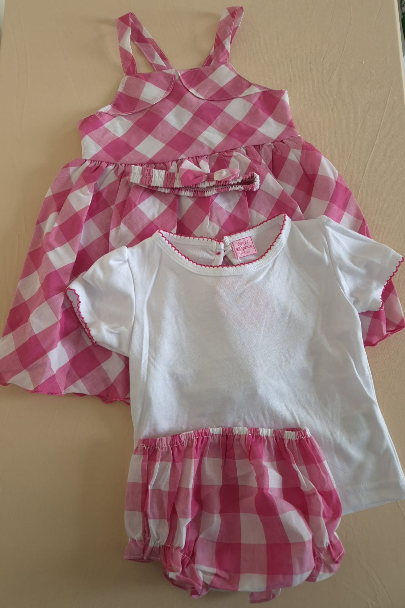 Pink and white checkered dress and bloomers set on a beige background